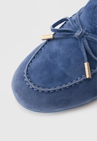 Sinise sametnahast mokasiin, kontrastse õmblusega, paindliku tallaga ja metallsete detailidega paelte juures. Sile tekstuur, ümar kuju.