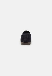 Mocasini din suede albastru marin cu un profil jos, spate rotunjit și cusături în contrast. Talpă plată din cauciuc pentru confort și ușurință în utilizare.