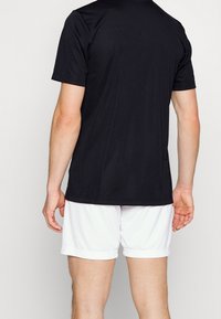 Svart kortärmad träningströja med en slät textur, bakvy, i kombination med vita shorts, som visar en enkel och funktionell design.