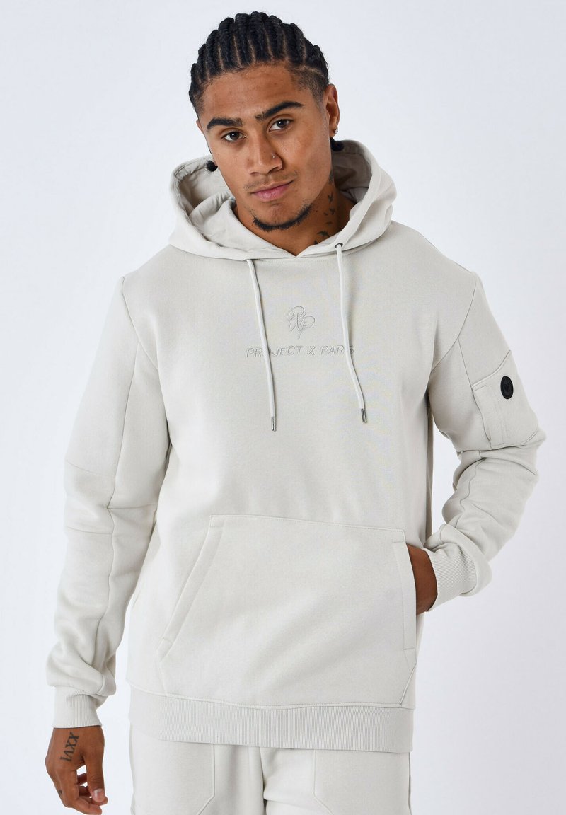 Sudadera gris claro hecha de tela suave, con un bolsillo frontal, capucha ajustable con cordón y logotipo bordado. Cuenta con un bolsillo lateral con un detalle de botón.