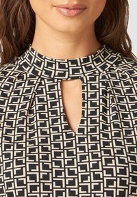 Black and cream top featuring a high neckline, keyhole cutout, and a geometric pattern with squares. Made of textured fabric.