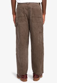 Brown cotton cargo pants with a relaxed fit, featuring multiple pockets on the back and sides, and a slightly worn texture.