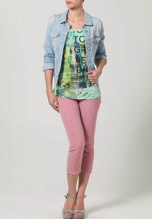 Lys denimjakke, grøn T-shirt med tekst, og lyserøde cropped bukser; grå høje hælede sandaler fuldender outfittet.