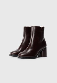 Une paire de bottines en cuir marron foncé avec des talons bloc et des orteils ronds sur un fond blanc.