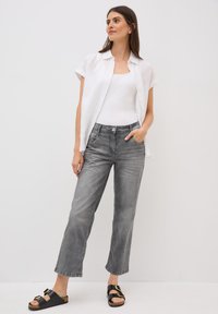 Pantalones anchos de mezclilla gris con un acabado desgastado, combinados con una camiseta sin mangas blanca y una camisa blanca suelta de botones. Sandalias negras con dos hebillas.