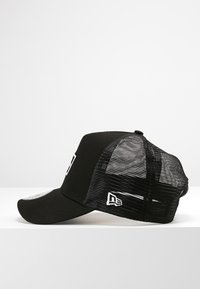 Black trucker cap with a solid front and mesh back, featuring a white logo and adjustable snap closure at the rear.