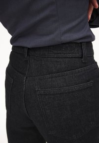 Mustad teksapüksid kõrge vöökoht, tekstuuriga kangas, minimalistlik disain ja nähtavad õmblused. Omab kahte tagataskut.