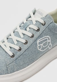 Baskets en denim bleu clair, avec des lacets blancs, des œillets ronds argentés, une semelle blanche épaisse et un logo discret sur le côté.