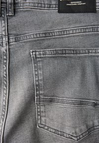 Vaqueros de denim gris con un único bolsillo trasero con costuras en contraste y una etiqueta negra en la cinturilla, que enfatizan la comodidad.