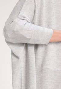 Ljust grå tröja med lös passform, rund halsringning och ärm-longd ärmar med finstickad textur och subtila ribbade detaljer.