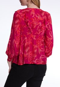 Fuchsie Bluse mit botanischem Druck, ausgestattet mit Rüschen entlang des Rückens und langen Puffärmeln, aus leichtem, fließendem Stoff gefertigt.