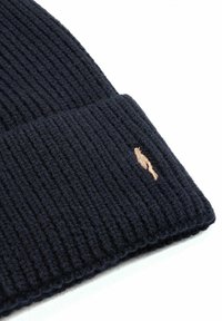 Granatowa dziana czapka beanie z ryflowanym wzorem i zawiniętą brzegiem. Posiada małe haftowane logo w jasnobrązowym kolorze z boku.