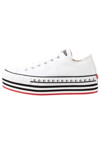 Vita canvas sneakers med svart och vit randig mellansula, röda sulkantoner och silverfärgade ögla. Har en vit gummitåspets.