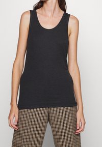 Svart ärmlös linne i lättviktigt tyg, med en rundad halsringning och en avslappnad passform. Matchas med byxor i brunt houndstooth-mönster.