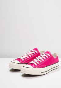 Baskets en toile rose avec semelles en caoutchouc blanc, rayure horizontale noire et lacets blancs ; bout arrondi et détails de surpiqûres en contraste.