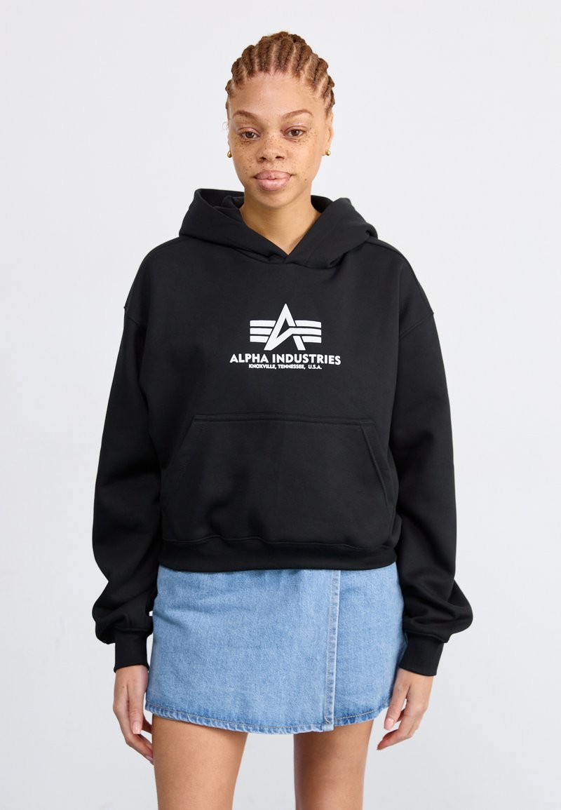 Čierna mikina s kapucňou a prednou kapsou, so bielym logom "Alpha Industries". Spárované so svetlomodrou džínsovou minisukňou.