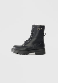 Botas de couro pretas com atacadores e sola grossa, apresentando uma corrente prateada decorativa na parte superior e uma alça na parte de trás.
