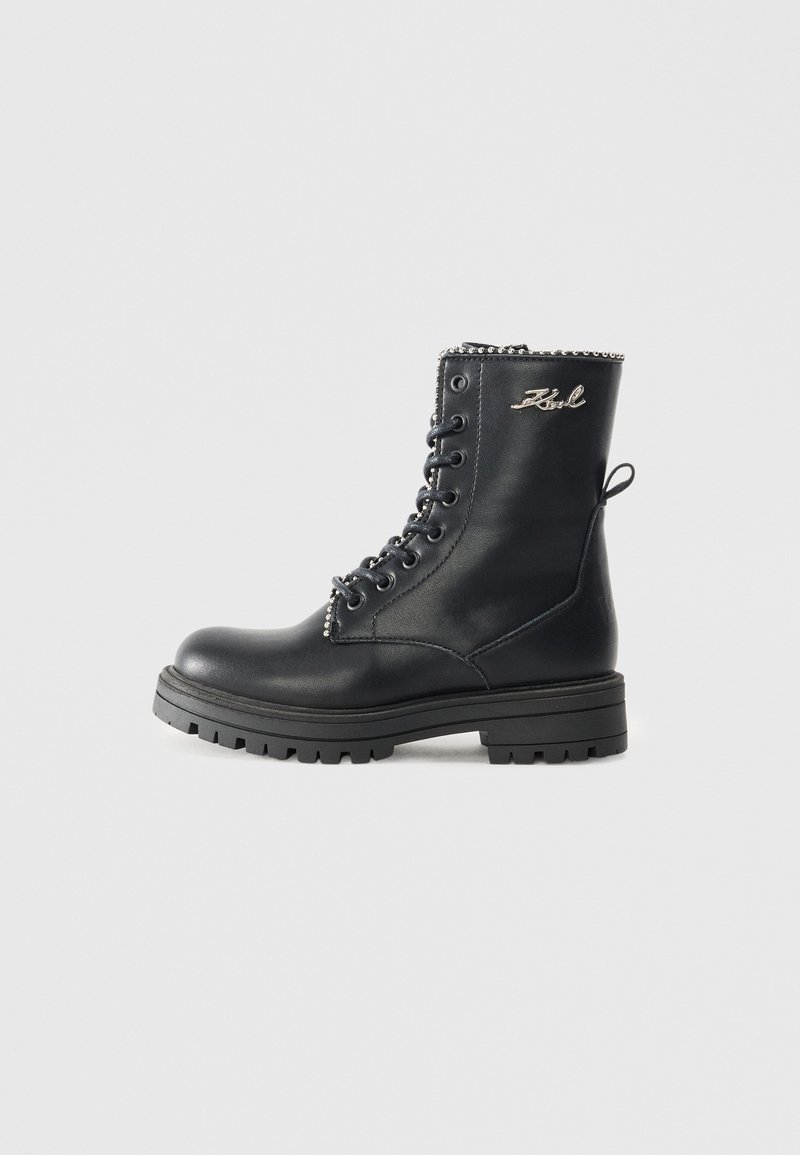Botas de couro pretas com atacadores e sola grossa, apresentando uma corrente prateada decorativa na parte superior e uma alça na parte de trás.