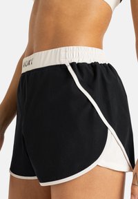 Zwarte sportshorts met een witte elastische tailleband, zijsplitten en een mesh voering. Heeft een contrasterende witte rand langs de randen.