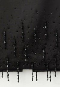 Textile noir présentant divers perles et embellissements noirs, y compris des formes allongées en goutte d'eau et des accents carrés, disposés dans un design en motifs.