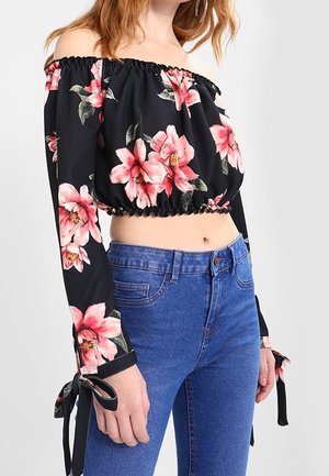 Top corto negro sin hombros con estampado floral rosa, escote fruncido, mangas largas con lazos, combinado con jeans de cintura alta azules.