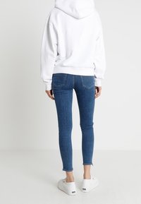 Jeans blu skinny con orlo sfilacciato, abbinati a un felpa con cappuccio bianca. L'outfit è completato da sneaker bianche.