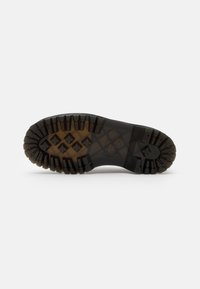 Semelle d'une botte en caoutchouc noir avec des crampons profonds comportant des motifs croisés et une adhérence robuste, présentée sur un fond blanc uni.