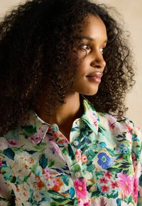 Camisa de botones con estampado floral en un tejido ligero y texturizado. Presenta una variedad de flores coloridas sobre un fondo claro.