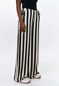 Zwart en beige gestreepte wijde broek met zakken, gemaakt van zachte stof; heeft een relaxte uitstraling en contrasterende horizontale strepen aan de onderkant.