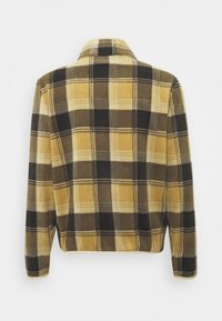 Långärmad jacka med ett rutigt mönster i gult, svart och brunt. Mjuk tygkvalitet, kragsdesign och rak fåll synliga.