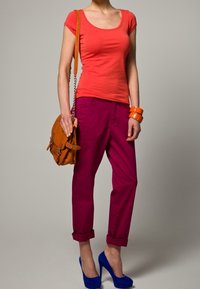 Camiseta roja de escote redondo, pantalones fucsias de puño enrollado, bolso naranja y tacones azules. Tela suave con un ajuste casual.