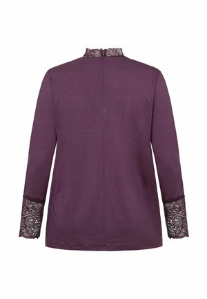 Lila hosszú ujjú felső csipke díszítéssel a mandzsettákon és a galléron, hátulról bemutatva, fehér háttérrel.