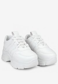 Las zapatillas blancas presentan un diseño voluminoso con una suela gruesa, paneles texturizados y un cierre de cordones. Están hechas de un material sintético suave.
