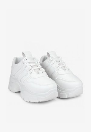 Las zapatillas blancas presentan un diseño voluminoso con una suela gruesa, paneles texturizados y un cierre de cordones. Están hechas de un material sintético suave.