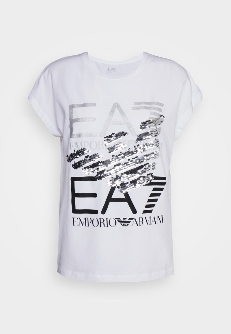 Vit t-shirt med kort ärm som har silver- och svart text med paljetter i en grafisk design. Texten lyder "EA7 EMPORIO ARMANI."