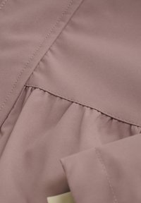 Lys mauve stof med en glat tekstur. Har samlet detaljer langs en indsyet søm, synlig syning og en foldet kant.
