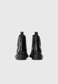 Black leather ankle boots with a smooth texture, elastic side panels, and pull tabs; features a low, textured rubber sole for grip.