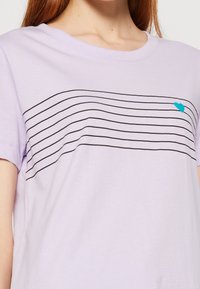 Lys lilla t-shirt med korte ærmer, sort vandrette striber og et lille turkist hjerte på venstre side. Blødt bomuldsstof.
