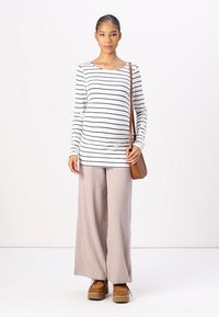 Weißes Langarmoberteil mit schwarzen Streifen, kombiniert mit hellrosa gerippten Weitbein-Hosen und braunen Schuhen. Eine braune Schultertasche rundet den Look ab.