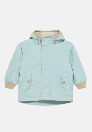 Ανοιχτό μπλε μπουφάν με κουκούλα, κλείσιμο με πατιλέτες και δύο μπροστινές τσέπες. Πλεκτά μανίκια σε μπεζ χρώμα και λείο, ανθεκτικό στο νερό υλικό.