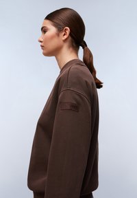 Brown crewneck sweatshirt met ribgebreide mouwen, een textuur patch op de linkermouw en een relaxte pasvorm. Gladde stof met een matte afwerking.