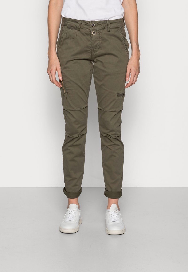 Pantalon cargo vert olive à coupe slim, doté d'une poche zippée, de panneaux latéraux et de revers roulés, associé à des baskets blanches.
