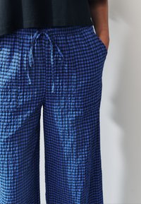 Pantalon à carreaux bleu en tissu léger, doté d'une taille à cordon, de poches latérales et d'une coupe décontractée, avec une texture froissée.