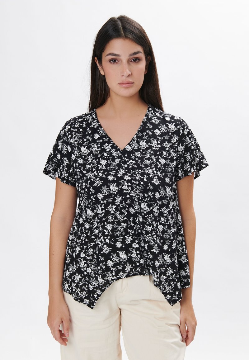 Sort blomsterbluse med korte ærmer, v-hals og en løs pasform. Har et delikat hvidt blomstermønster og en ujævn kant.