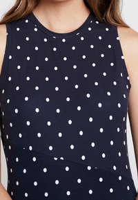 Námořnické bezramínkové šaty s bílými puntíky, kulatým výstřihem a hladkou texturou látky, mají přiléhavý střih a detail bočního švu.