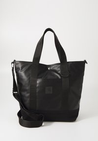 Sac fourre-tout noir en matériau lisse, avec une poche carrée à l'avant, des poignées courtes doubles et une bandoulière amovible.