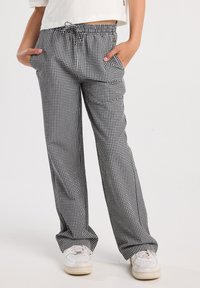 Black and white gingham patterned pants with an elastic waistband, drawstring, and side pockets, paired with white sneakers.