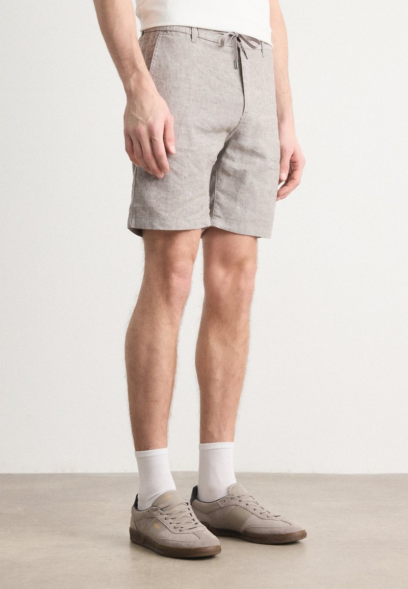 Gray linen shorts with a drawstring waistband, a straight cut, and side pockets, paired with white socks and gray sneakers.