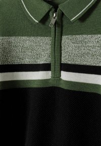 Poloshirt mit Reißverschluss, das grüne, weiße und schwarze Streifen hat. Strickstoff mit strukturierter unterer Sektion. Enthält einen spitzen Kragen und silberne Hardware.