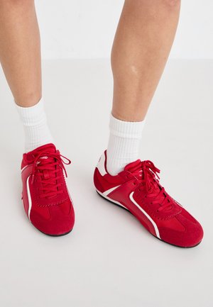 Scarpe da ginnastica rosse con accenti bianchi, realizzate in suede e rete. Presentano un design con lacci e suole testurizzate per una migliore aderenza.